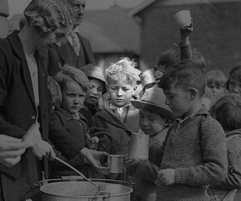 Schoolchildren line up for free issue of soup and a slice of bread / 1934