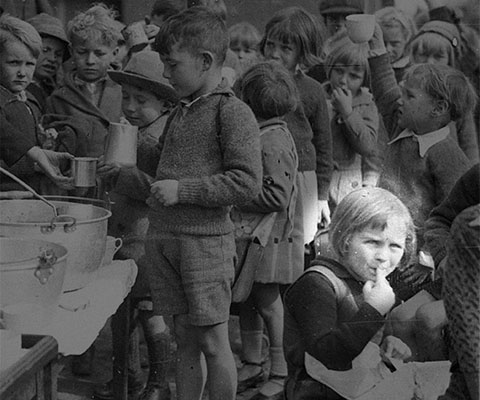 Schoolchildren line up for free issue of soup and a slice of bread / 1934